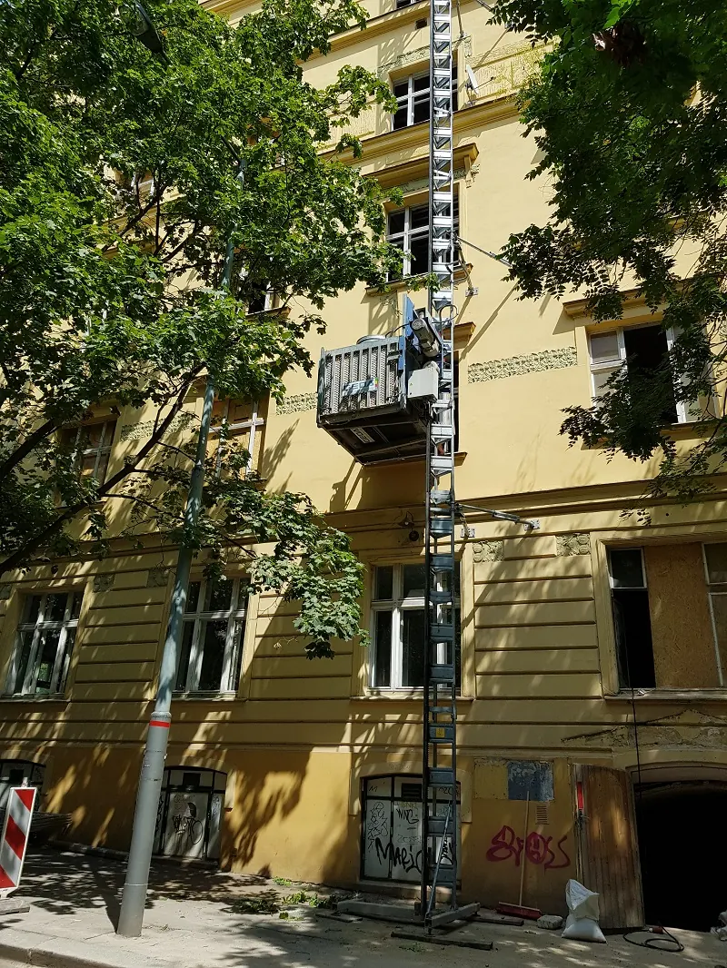 Stavební výtah GEDA 500 NeloSTAV na žluté fasádě domu v Mánesově ulici